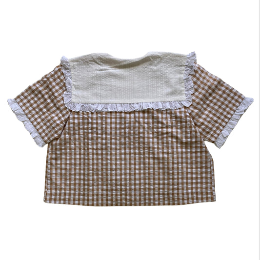 Checkered shirt with white collar and lace ruffles on a white background. Seersucker organic cotton top.