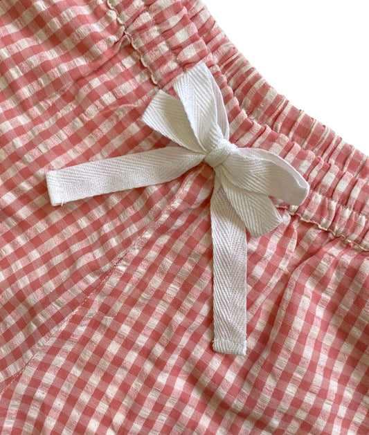 Close-up of a pink and white checkered short with a white ribbon bow on a matching background. Pink gingham shorts with lace.