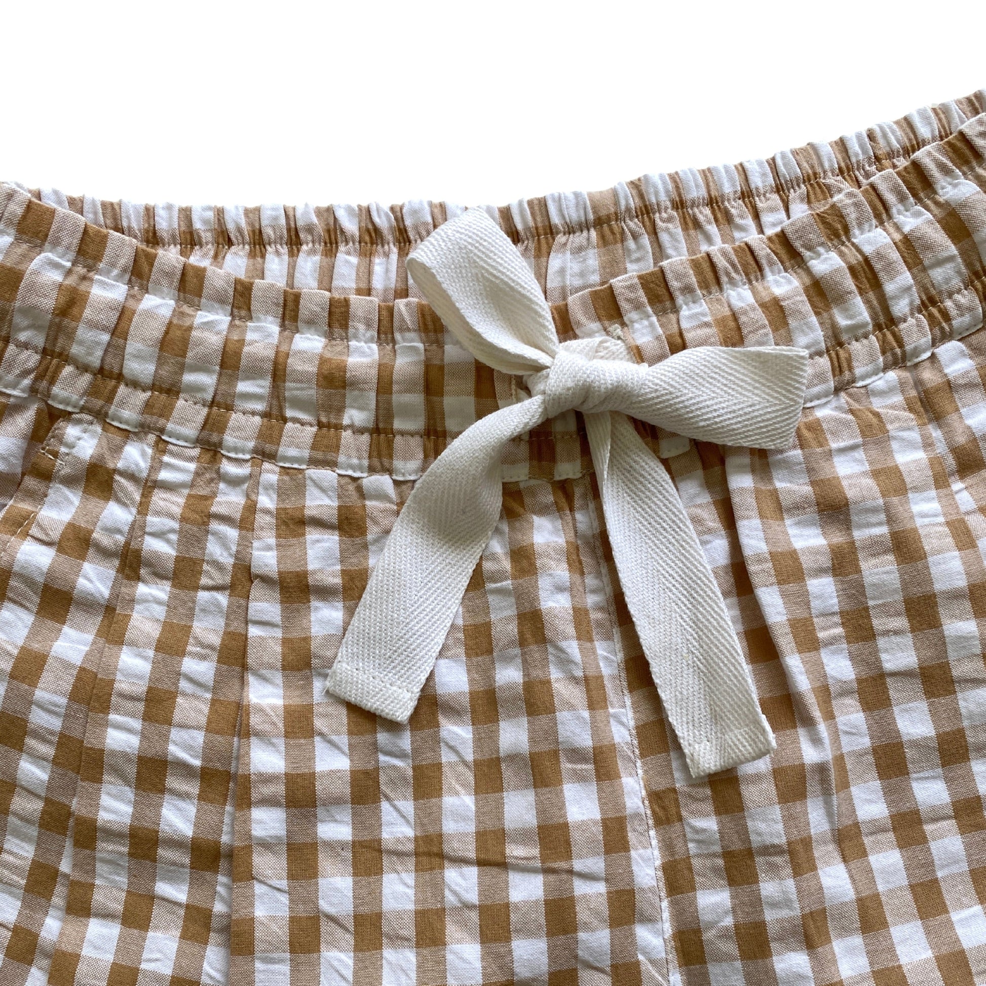 Brown and white checkered shorts with a tie waist on a white background. Twill tape bow tie. Gingham shorts.