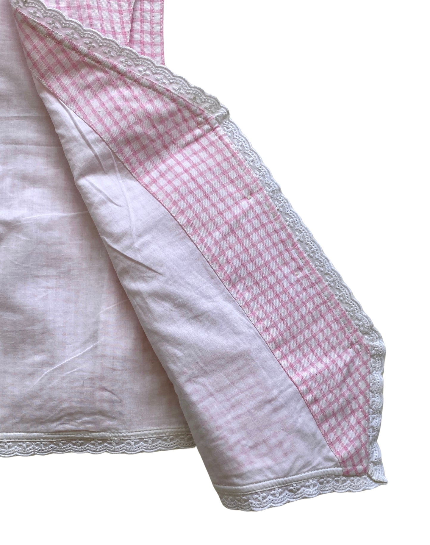 Close-up of a waistcoat with pink checkered border and white lace trim and inside lining on a white background