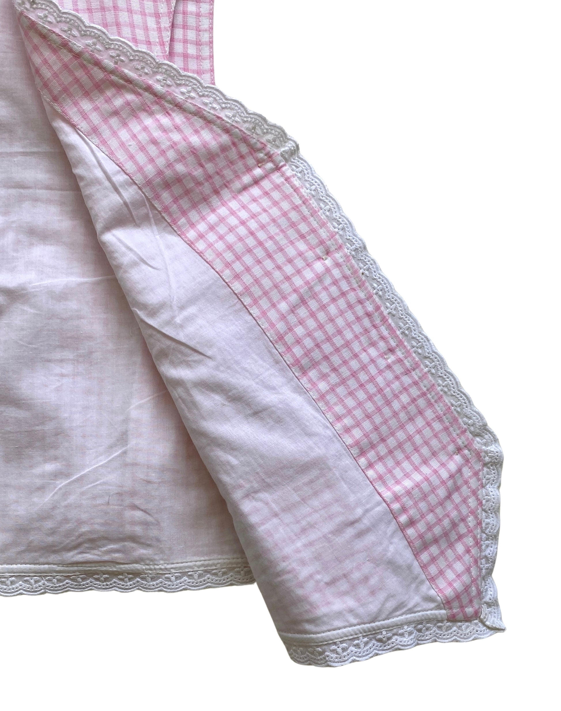 Close-up of a waistcoat with pink checkered border and white lace trim and inside lining on a white background