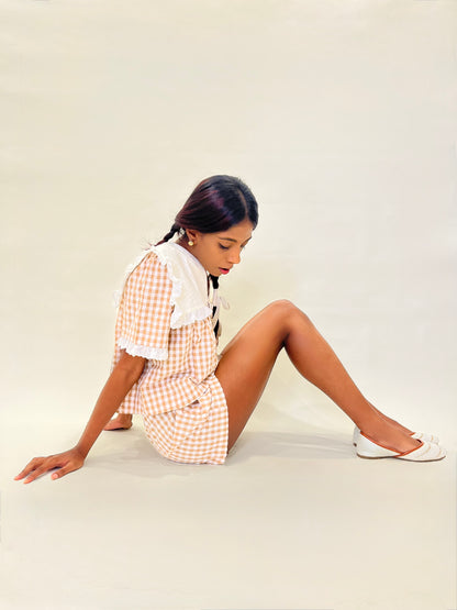 Model in a checkered co-ord brown gingham set sitting on a white surface