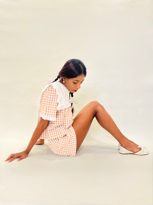 Model in a checkered co-ord brown gingham set sitting on a white surface