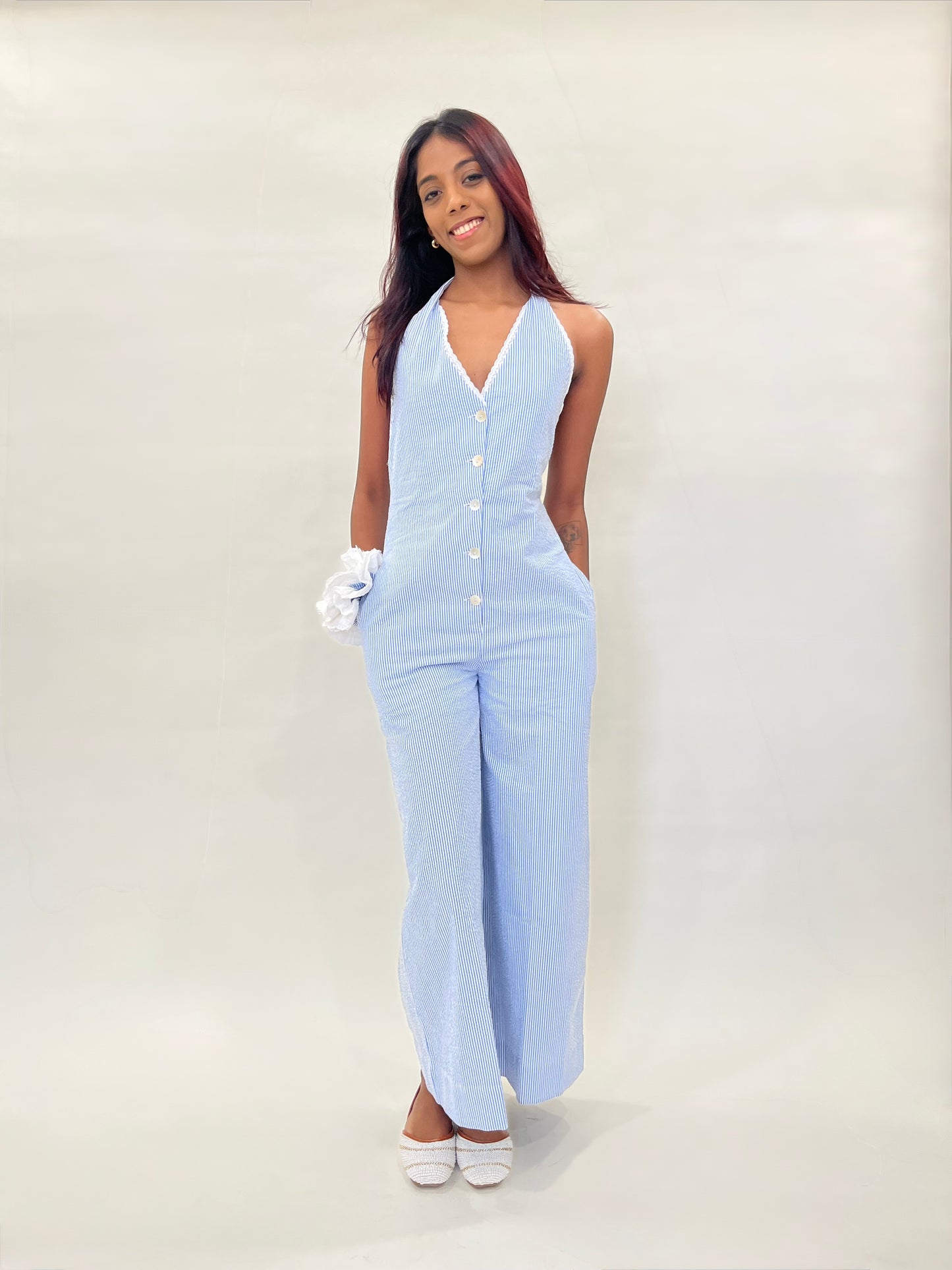 Model wearing a light blue striped seersucker jumpsuit with lining against a white background. Organic cotton fabric with shell buttons.