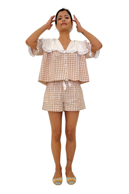 Woman wearing a checkered outfit with a white lace top on a white background. Brown gingham set.