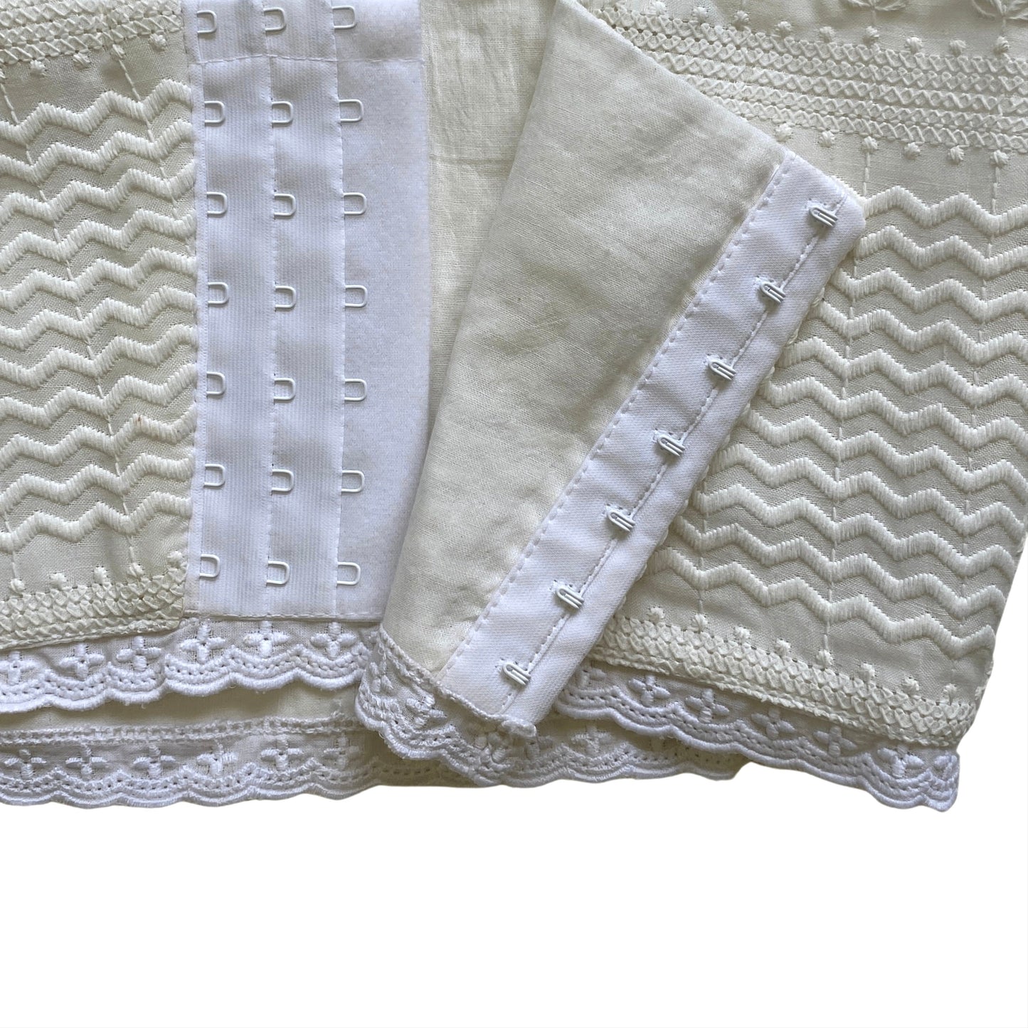 Close-up of a textured corset in white fabric with lace trim on a white background. Bree hook & eye clasp closure.