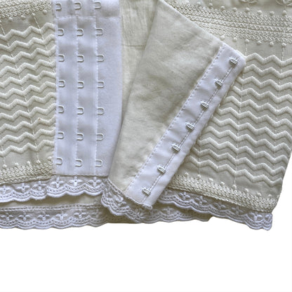 Close-up of a textured corset in white fabric with lace trim on a white background. Bree hook & eye clasp closure.