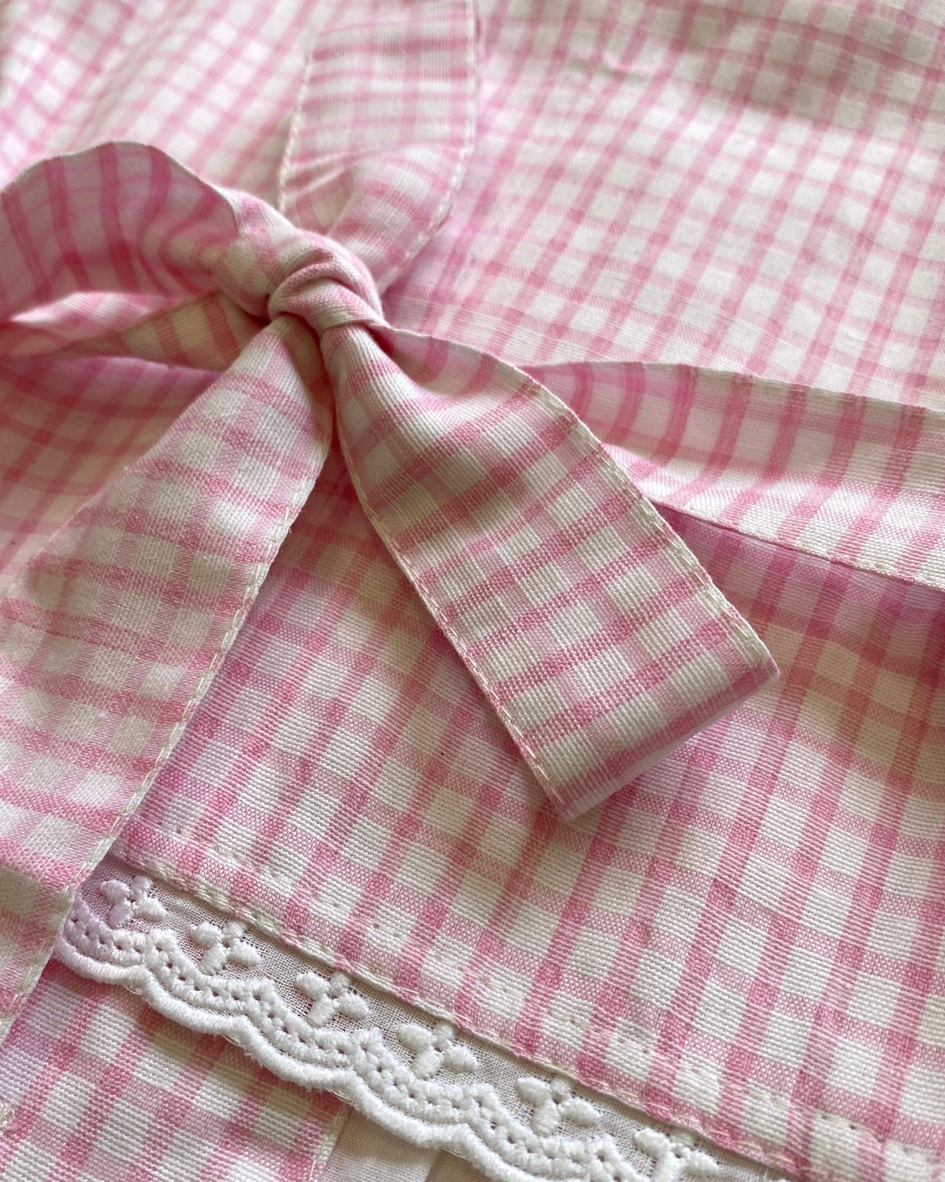 Close-up of pink and white checkered waistcoat with a lace trim and back bow