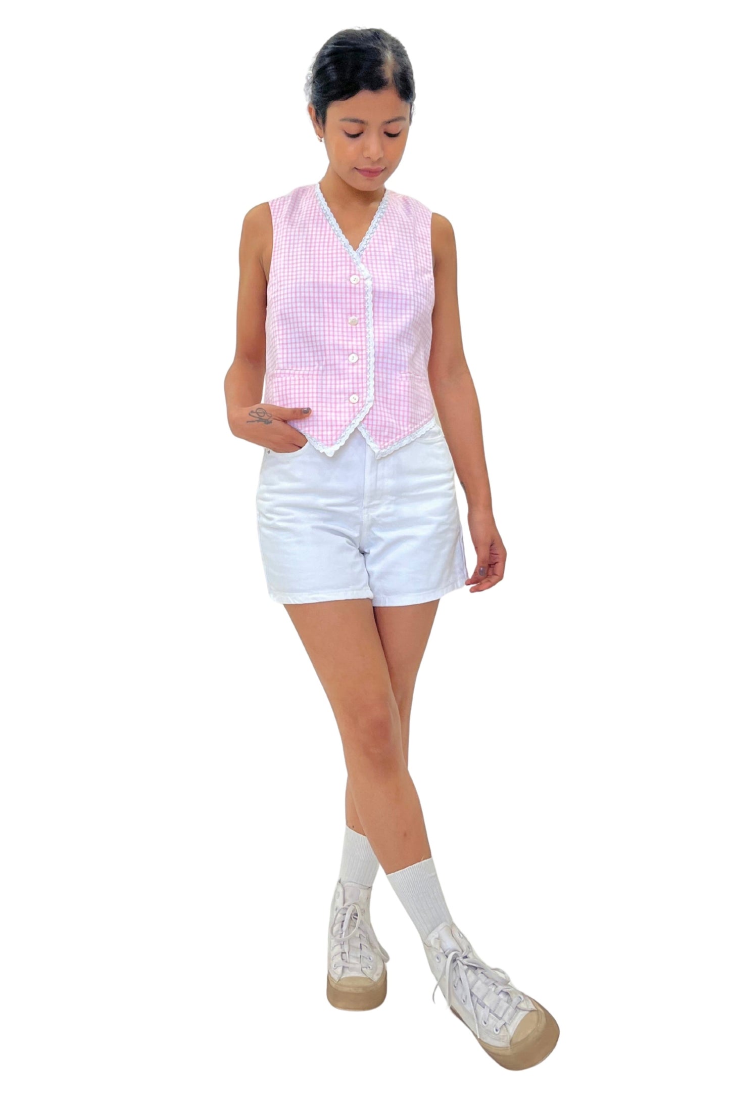Person wearing a pink checkered vest, white shorts, and white shoes on a white background