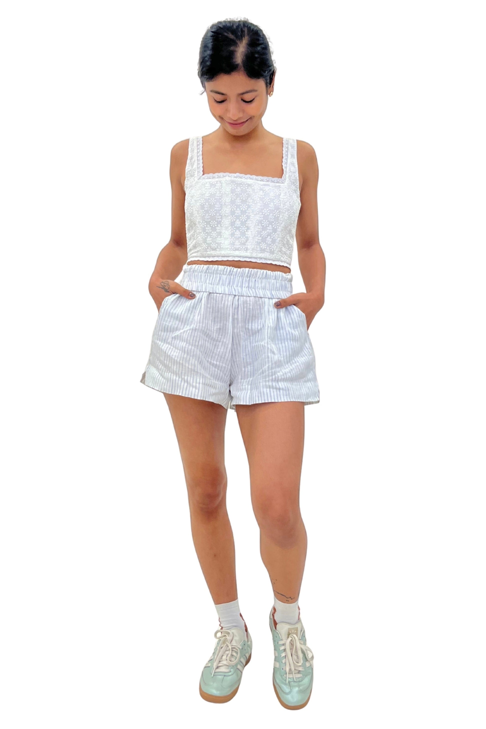 Woman wearing a white embroidered corset and white striped linen shorts on a white background