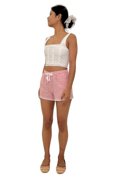 Woman wearing a white sleeveless top and pink checkered shorts on a white background