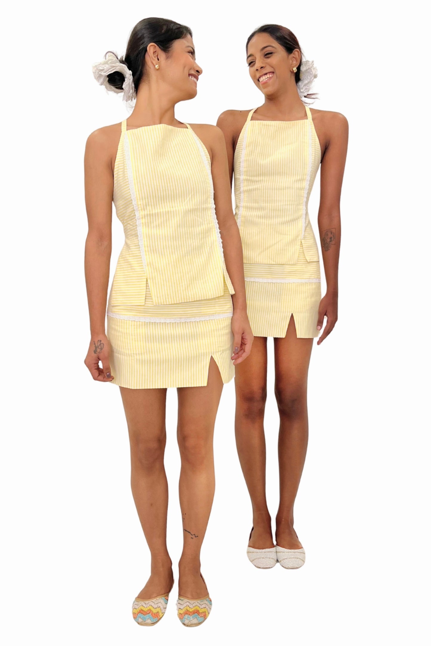 Two women wearing matching yellow outfits on a white background. Seersucker yellow and white striped top and skirt set.