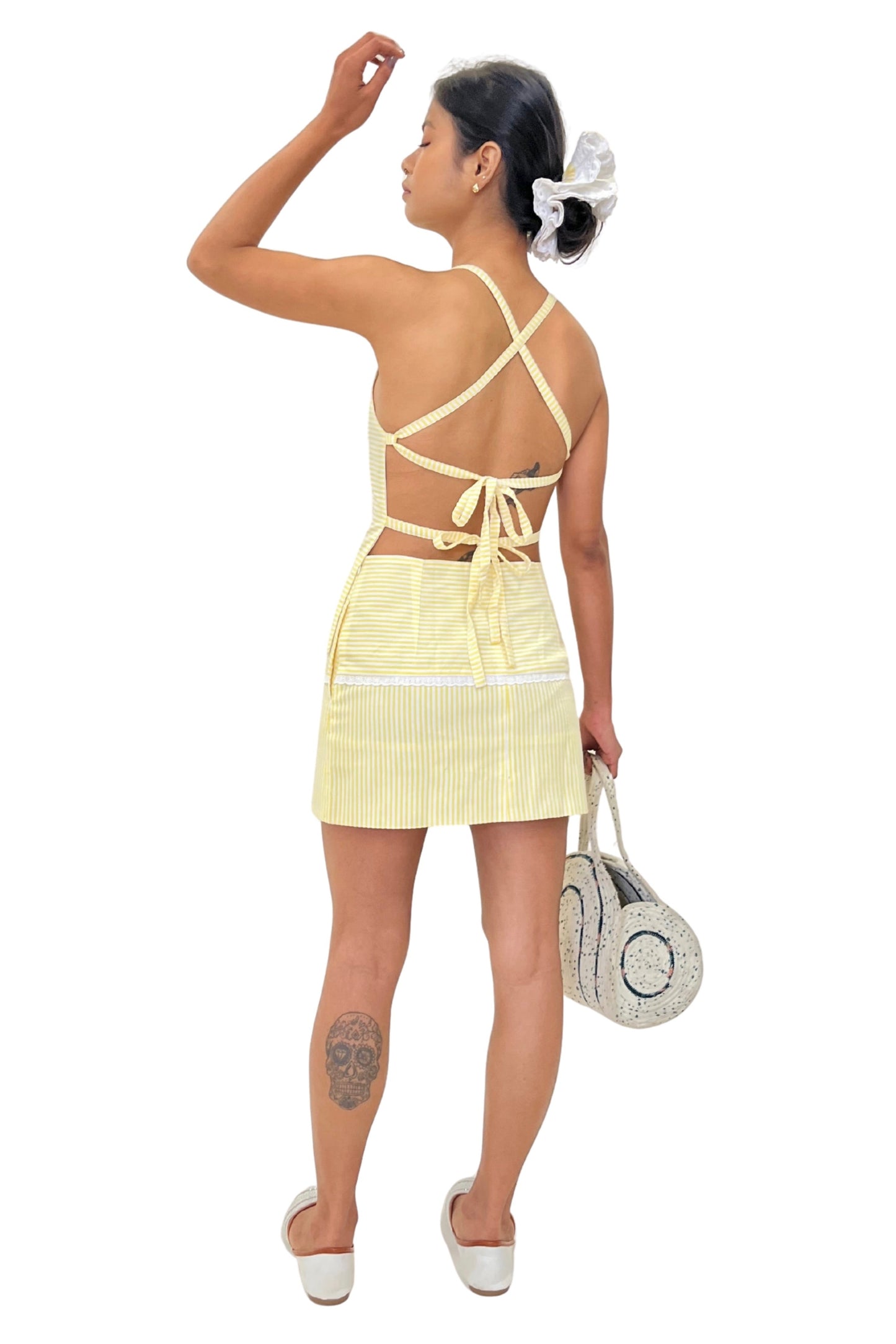 Woman wearing a top and skirt set with thin straps & open back holding a white bag on a white background